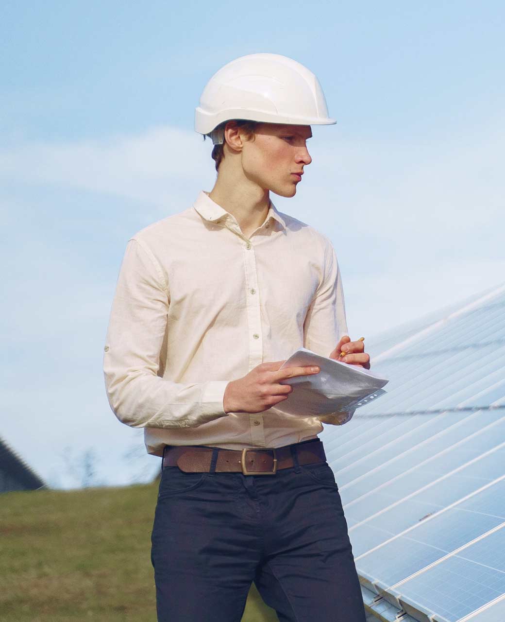 A man in a hard hat is holding a tablet in front of solar panels.