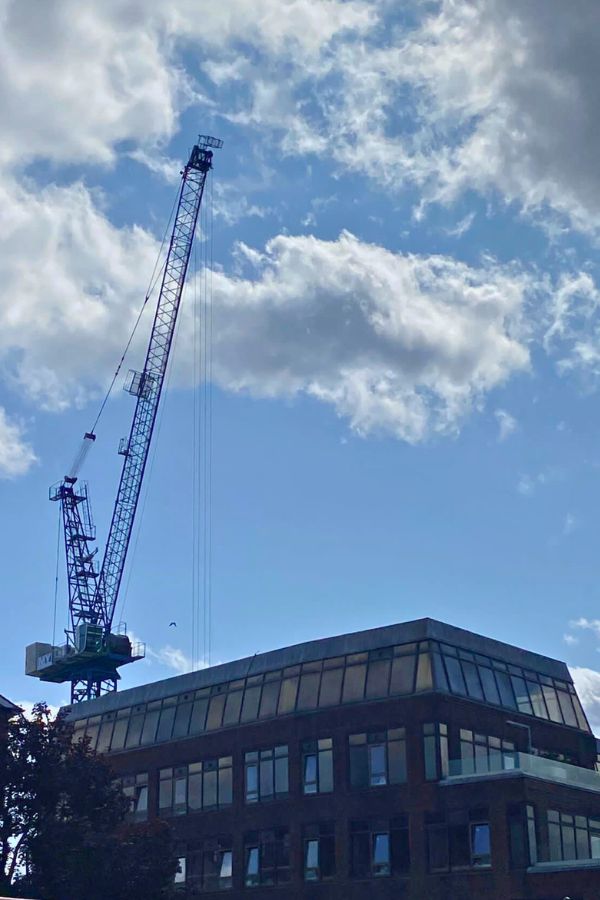 A crane sits on top of a building with clouds in the sky.